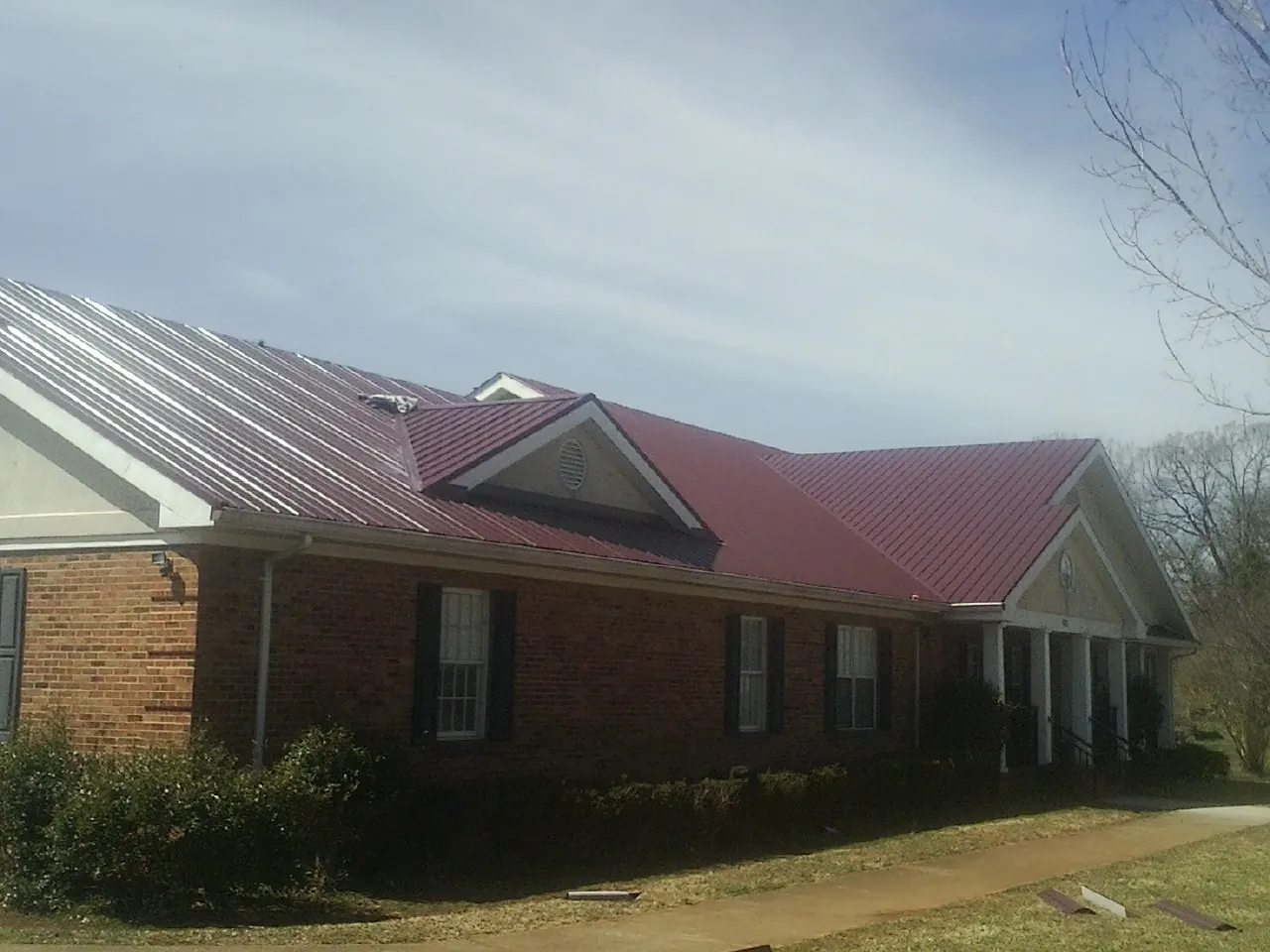 Red metal roof with gabled entries on a long brick building, from a Hail Damage Roof Repair job in Fordyce