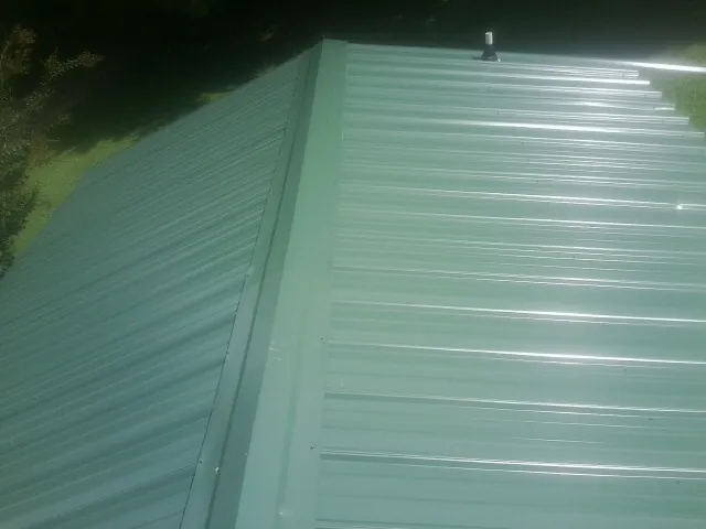 New green metal panels meeting at the ridge of a roof — Flat Roof Repair work by our crew in Fordyce
