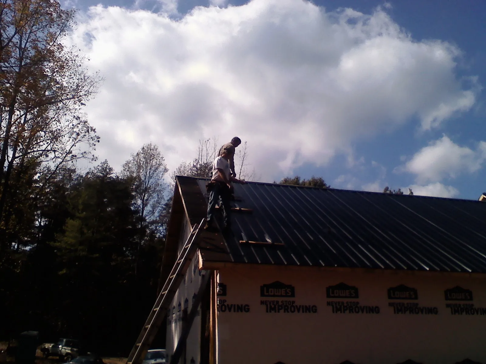 Roofer fastening dark metal panels high against a cloudy sky, from a Roof Inspection job in Fordyce