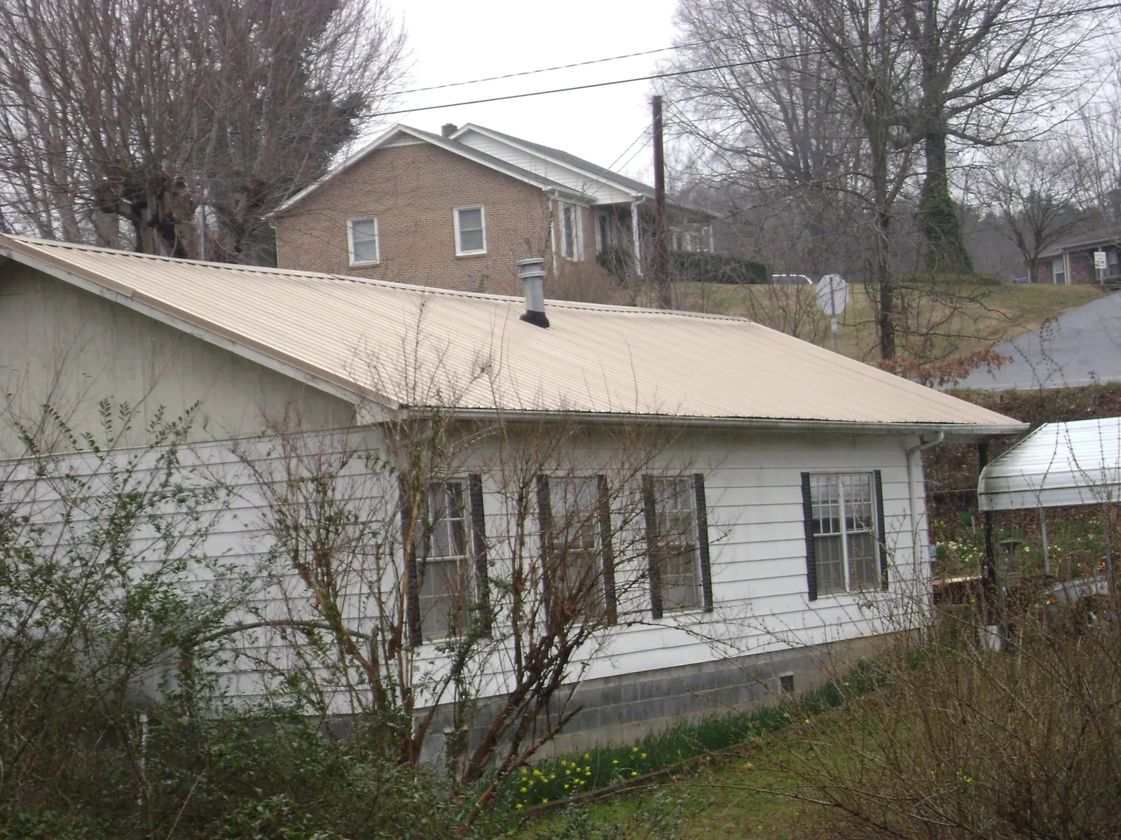 Tan metal roof on a white sided house set into a hillside — Commercial Roofing by Roofing Brothers in Fordyce